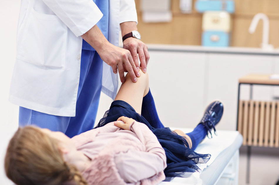 Ein Orthopädie untersucht das Knie eines Mädchens.