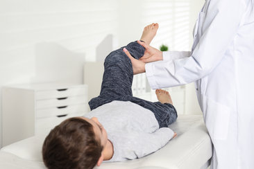 Kinderorthopäde bei der Untersuchung. Kinderorthopädische Krankheitsbilder an der Hüfte sind zum Beispiel Hüftdysplasie, Hüftluxation, Hüftkopfnekrose (Morbus Perthes) Wachstumsfugenlösung/Hüftkopfgleiten (Epiphyseolysis capitis femoris)
